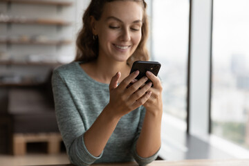 Fototapeta na wymiar Crop close up of smiling millennial Caucasian woman hold smartphone text message on modern device online. Happy young female look at cellphone screen browse wireless internet. Technology concept.