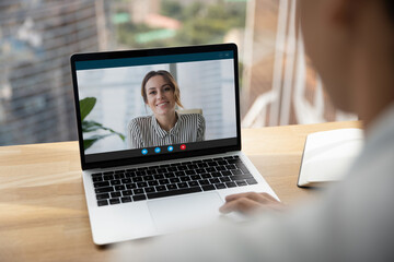 Rear over shoulder view of man talk speak with smiling female colleagues on video online call on laptop. Diverse businesspeople have webcam digital virtual zoom meeting. Communication concept.