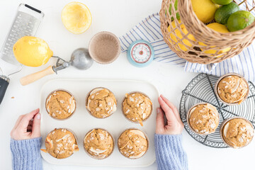 White ceramic tray with six fresh cocoa muffins held by two woman hands next to a cooling rack with another three delicious just baked muffins.