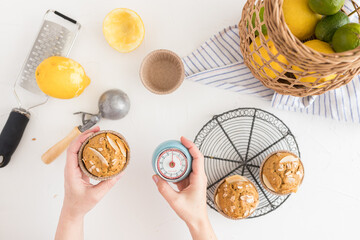 Woman hands holding a retro analog timer with one hand and a just baked cocoa muffin with the other.