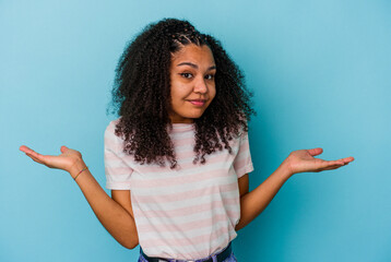 Young african american woman isolated on blue background doubting and shrugging shoulders in...