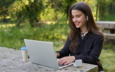 long-haired pretty businesswoman with laptop, headphones and coffee at stone table. teenager...