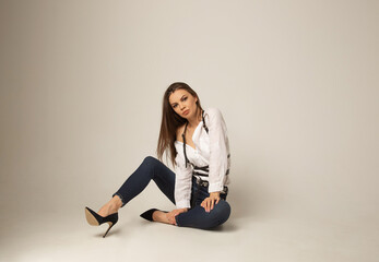 Portrait of young caucasian brunette woman in a white blouse, jeans and harness