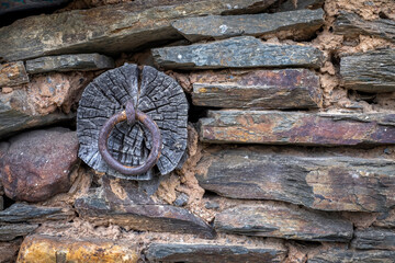 Fototapeta na wymiar detail of a slate building with slate stones, mud adobe and a wooden beam with a nail and a rusty ring hanging down, rural texture