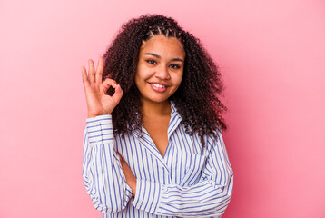 Young african american woman isolated on pink background winks an eye and holds an okay gesture with hand.