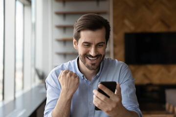 Happy young male triumph read promotion email or message on smartphone gadget. Smiling millennial...