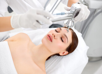Cosmetologist treating face of woman with laser machine