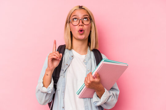 Young venezuelan student woman isolated on pink background pointing upside with opened mouth.