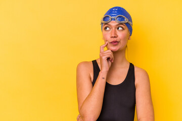 Young swimmer venezuelan woman isolated on yellow background looking sideways with doubtful and skeptical expression.