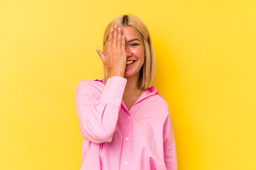 Young venezuelan woman isolated on yellow background having fun covering half of face with palm.