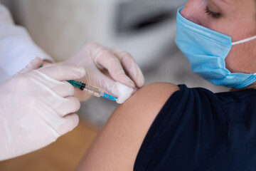 Coronavirus vaccination, doctor injecting a patient, getting first shot of covid vaccine in arm muscle. Medical doctor in protective suit and mask, process of immunization against covid-19