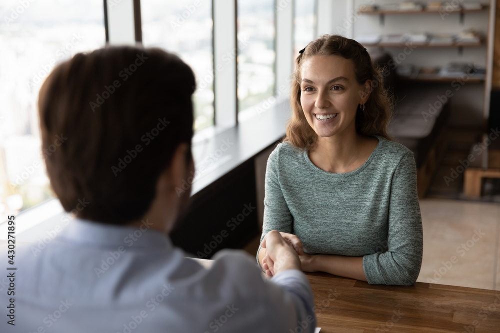 Wall mural Smiling female employee shake hand of male employer or recruiter get acquainted greet at meeting in office. Happy woman handshake business partner closing deal or making agreement at negotiation.