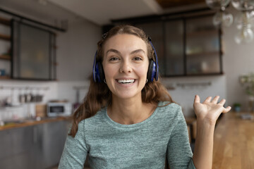 Headshot portrait of smiling young Caucasian woman in headphones wave greet talk on video call...