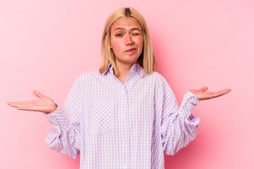 Young venezuelan woman isolated on pink background doubting and shrugging shoulders in questioning...