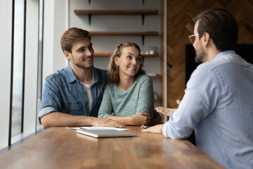 Happy couple clients talk speak with male relator or broker at office meeting, plan buying home...