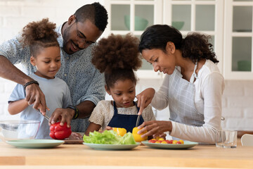 Happy family couple teaching two preschooler kids preparing salad. Parents and children cooking dinner together in kitchen, slicing fresh vegetables. Organic food, healthy vegetarian nutrition concept