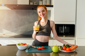 Athletic woman with gym clothes drinks orange fruit in the kitchen