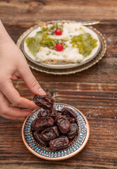 Fresh date fruits in ottoman handmade bowl on the front and Traditional Turkish milky Ramadan Dessert named Gullac on the background. White wooden background. Ramadan (Ramazan) food for iftar or sahur