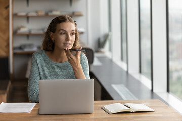 Young Caucasian businesswoman sit at desk in office work online on computer record audio voice...