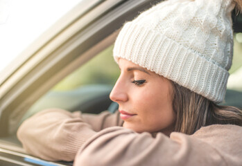 A young girl rests leaning against a car window. She is relaxing in the sun. She looks happy. Travel and vacation concept.