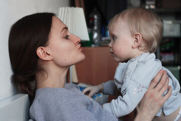 A young mother is kissing her little blonde daughter. Woman and baby. Unconditional love. Pastime...