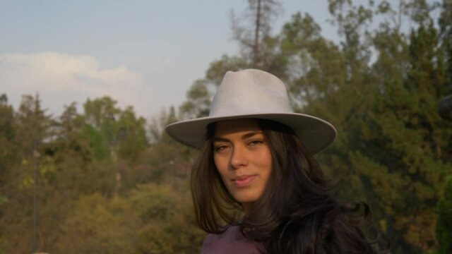 A shallow focus of a young brunette Hispanic woman with a fedora hat in a park shot in 4K