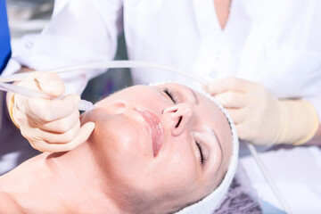 Mature woman having jet peeling face treatment in the clinic 
