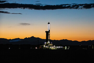 Obraz premium A oil and gas drilling/fracking operation and the front range of the Rocky Mountains, silhouetted by the sunset - East of Denver, Colorado