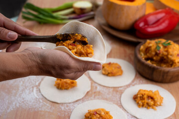 hands making the repulgue and closing of homemade Argentine empanadas and in the background empanadas finished with vegetables and filling on wooden table