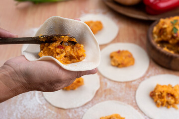 hands making the repulgue and closing of homemade Argentine empanadas and in the background empanadas finished with vegetables and filling on wooden table