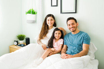 Obraz premium Cheerful parents and daughter smiling in bed