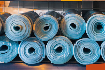 New rolled up yoga and fitness mats on a store shelf. Accessories or attributes for sports and a...
