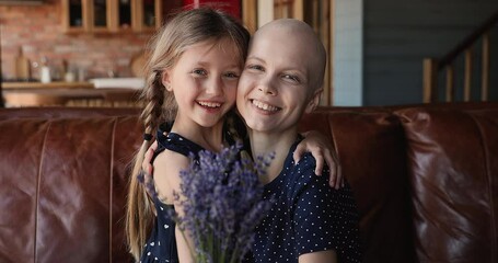 Happy bonding young woman with hairless head having cancer cuddling small child daughter, showing lavender flowers to camera, celebrating remission, feeling hopeful and inspired for oncology fight.