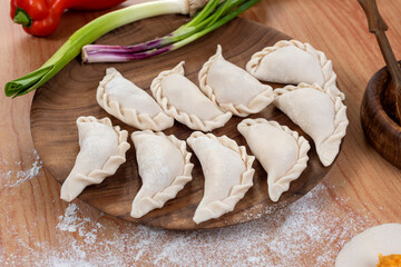 Argentine raw empanadas on round wooden plate on wooden table top with flour decorated with vegetables