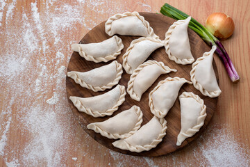 Argentine raw empanadas on round wooden plate on wooden table top with flour decorated with vegetables