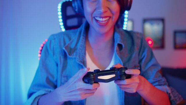 Happy asia girl gamer wear headphone set and joystick controller talk with friend feel fun and excited with competition online game in neon living room home studio at night, Home quarantine activity.