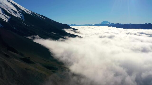 Aerial shot above low lying clouds in Chilean National Park Vicente Perez Rosales showing snow peaked mountains.