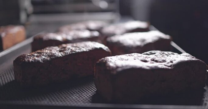 Fresh hot bread comes out of the oven on a conveyor belt. Baker  is spraying breads with water to add gloss and shine.