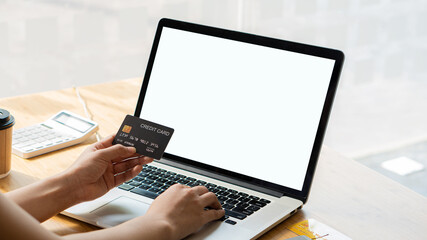 A young woman holds a plastic credit card on her computer in online purchases and online payment sites.