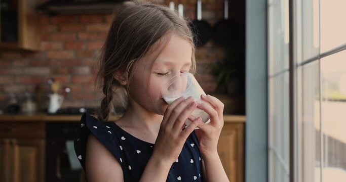 Head shot funny cute little 7s kid girl drinking glass of sweet organic yoghurt in morning looking at camera showing milk mustache, enjoying healthy beverage, children healthcare lifestyle concept.