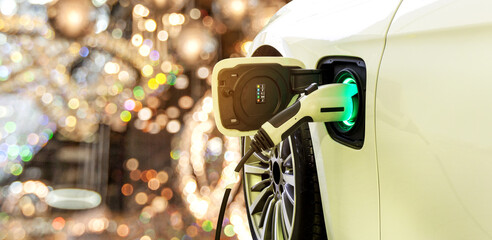 EV Car or Electric car at charging station with the power cable supply plugged in on blurred Night cityscape background.	