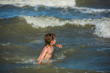Kid boy playing and having fun on the beach on blue sea in summer. Happy child playing in the sea.