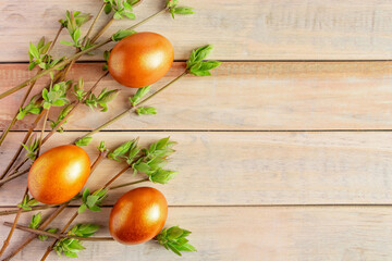 Golden Easter eggs and green willow buds on a wooden background.