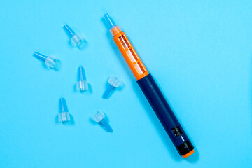 Insulin syringe pen with specialized needles scattered around to give injection to person with diabetes. blue background, top view, copy space. Equipment for providing specialized first aid.