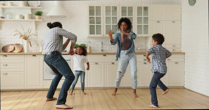 Full length happy active two generations african ethnicity family having fun together in modern bright kitchen, dancing to favorite energetic disco music, enjoying carefree leisure pastime at home.