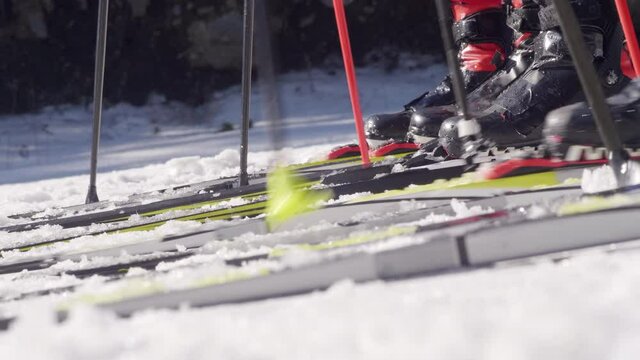 Close up shot of legs of unrecognizable skiers preparing and then start skiing with poles on snow on winter day
