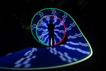 Obraz premium One person standing alone against a Colourful circle light painting as the backdrop 