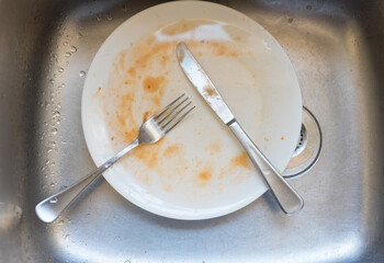 High angle view of dirty plate and knife and fork in sink (selective focus)