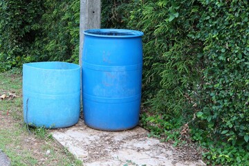 Two large blue plastic trash cans are located on an outdoor pavement area for littering.