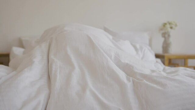 Attractive blonde in pink pajamas hiding under the covers in bed in her bedroom
